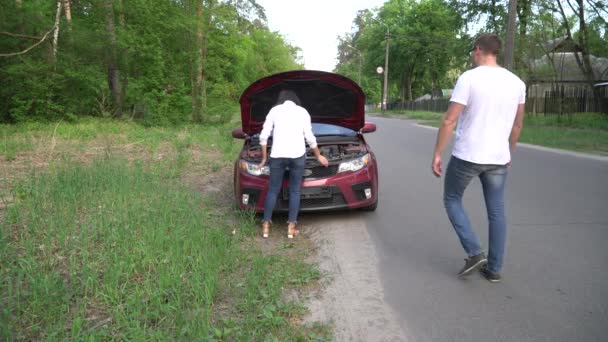 Man hjälper kvinnan med sin trasiga bil mitt i en landsbygd. — Stockvideo