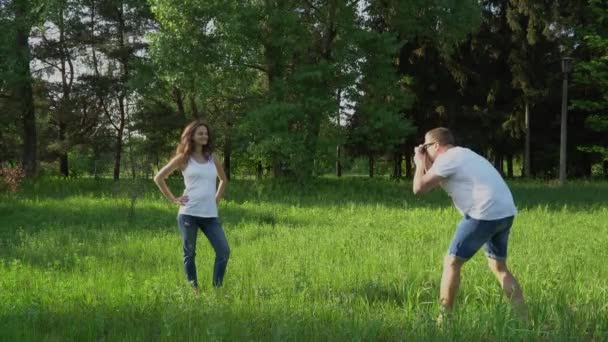 Hombre guapo toma fotos con la cámara de la joven embarazada feliz en el parque — Vídeos de Stock