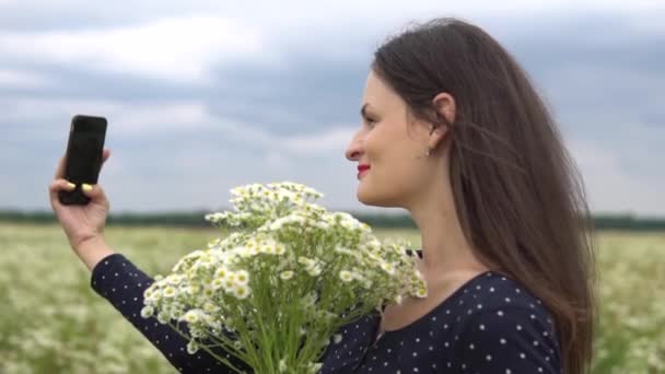 Hermosa chica haciendo selfie, foto con flores de manzanilla afuera . — Vídeo de stock