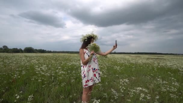 Hermosa chica embarazada haciendo selfie, foto con flores de manzanilla afuera . — Vídeos de Stock