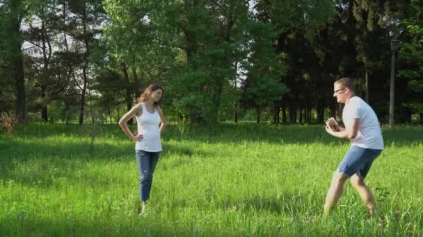 Handsome man takes photos with camera of young happy pregnant woman in park — Stock Video