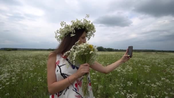 Hermosa chica embarazada haciendo selfie, foto con flores de manzanilla afuera . — Vídeos de Stock
