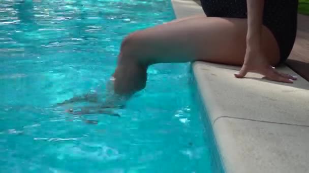 Eine schöne schwangere Frau mit einteiligem Badeanzug sitzt in der Nähe des Pools. — Stockvideo