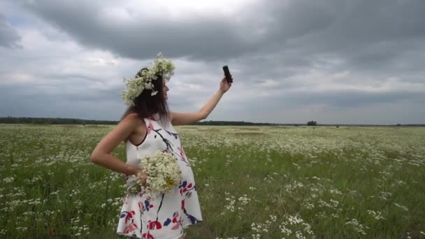 Όμορφη έγκυος κορίτσι κάνει selfie, φωτογραφία με λουλούδια χαμομήλι εκτός. — Αρχείο Βίντεο