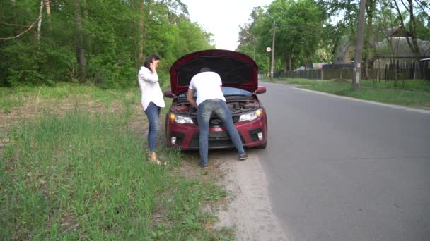 Man is het helpen van de vrouw met haar gebroken auto midden in een landschap. — Stockvideo