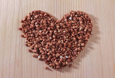 Karabuğday taneleri tahta bir arka planda kalp şeklinde serilirler. Kavram: Sağlıklı yemek.