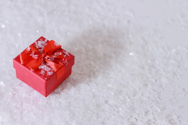 A small red box with a red bow with a gift on artificial snow. Concept: surprises and gifts for the winter holidays.