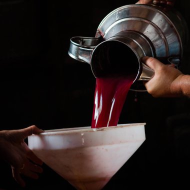 Üzüm hasadı, bir adamın elleri çelik bir testiden beyaz bir huniye üzüm jölesi döker..