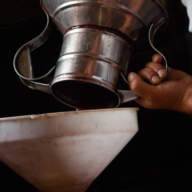 Üzüm hasadı, bir adamın elleri çelik bir testiden beyaz bir huniye üzüm jölesi döker..