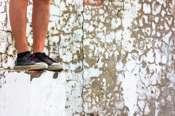 Gençlerin, eski püskü duvar arka planında yüksek bir duvarda bacakları çizilmiş. Yalnızlık. Zor yaş