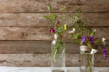 Çayır çiçekleri cam kavanozlarda buketler ve ahşap kırsal arka planda şişeler. Mesaj için yer var. Bitkisel tıp ve fizyoterapi konsepti. Country tarzı yaşam konsepti.