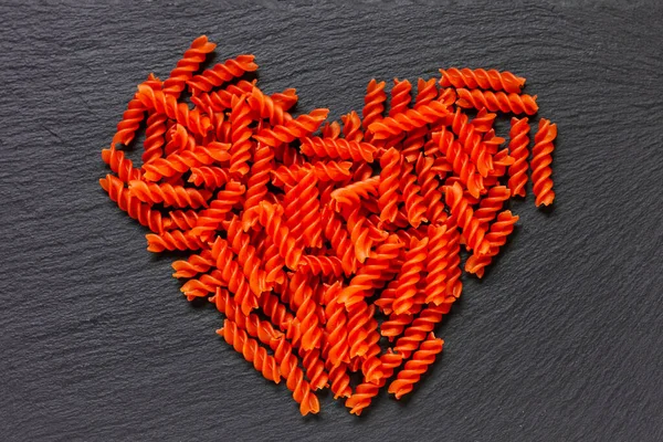 Heart-shaped organic red lentil pasta on rustic black backgrond. I love to be vegan. Gluten free. Top view.