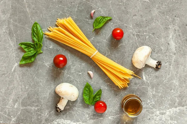 Mantarlı makarna malzemelerinin üst görünümü: spagetti, fesleğen, sarımsak, kiraz ve gri taş zemin üzerinde zeytinyağı