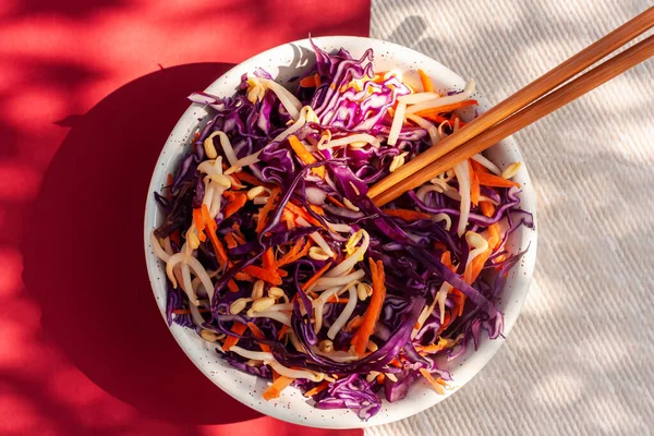 Kırmızı lahana salatası, beyaz ve kırmızı arka planda çubuklarla bezelye filizi ve havuç. Sağlıklı beslenme, vegan gıda konsepti. Üst görünüm.