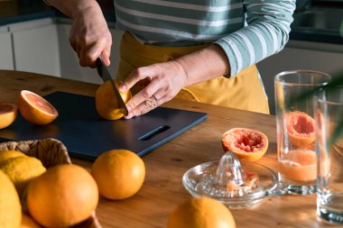 El yapımı narenciye sıkacağı ile ev yapımı greyfurt suyu yapan kadın elleri. Anonim bir kadın taze greyfurt suyu hazırlamak için olgun greyfurtu ikiye bölüyor..
