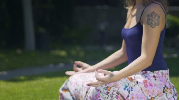 美丽的女人与纹身坐在莲花姿势深深沉思的户外公园 — 图库视频影像