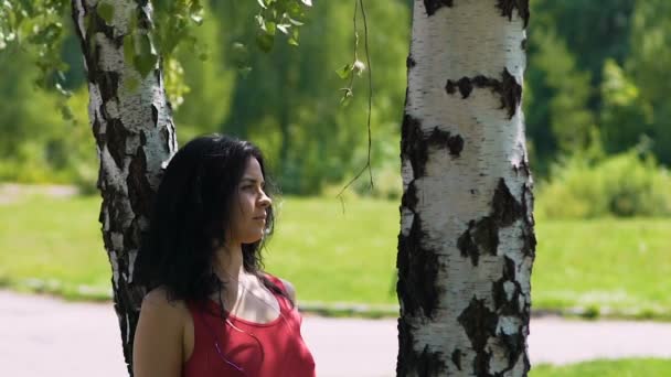 日付パートナーを待っている公園で白樺のツリーの下に立っている赤いドレスを着た女性 — ストック動画