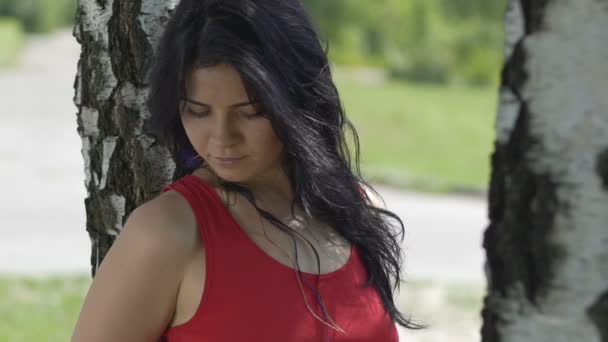 屋外日付のパートナーを待っている公園の木の下に立っている魅力的な強い女性 — ストック動画