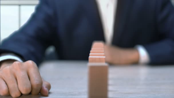 Podnikatel tlačí Domino, což způsobuje pád všech bloků, řetězovou reakci — Stock video