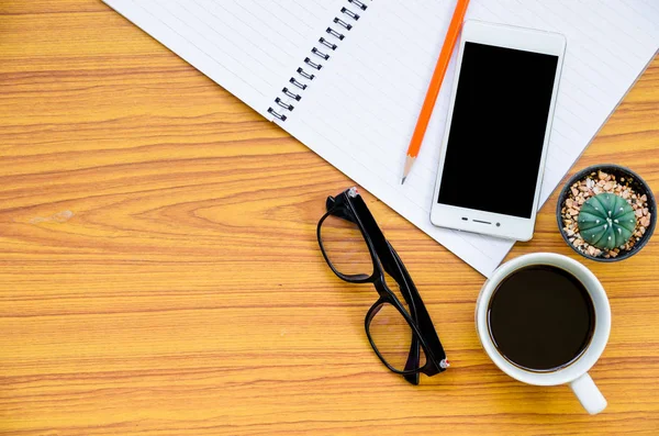 kahve fincanı, telefon, gözlük ve kaktüs üst sol boşluk görünümle ahşap masa üstünde defter