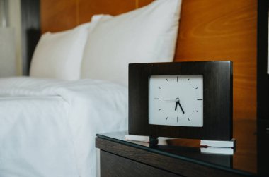 Beyaz yatağın yanında siyah saat