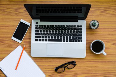 üstünde kahve fincanı, telefon, kitap, bardak ve kaktüs olan ahşap masa.