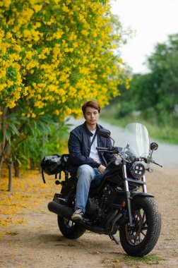 Asyalı genç adam kruvazör motosikletinin üzerinde oturuyor.