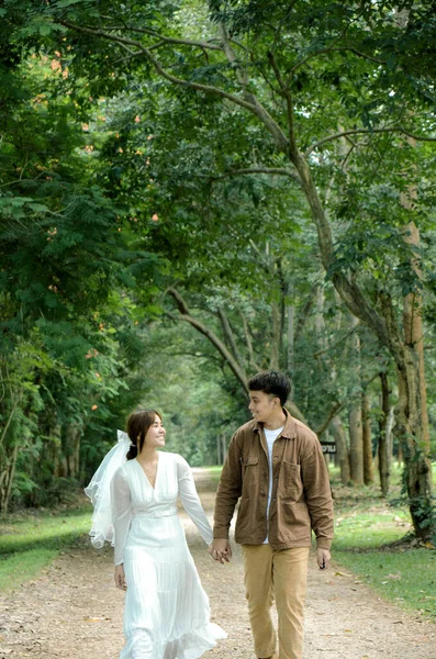 asian couple are walking and holding hand together on road with tree background