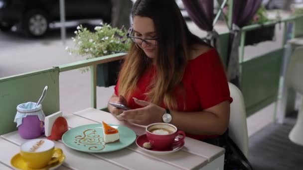 Menina bonito se comunica em um smartphone em uma mesa em um café — Vídeo de Stock