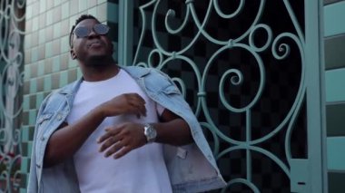 Siyah gözlüklü ve beyaz tişörtlü dans eden Afrikalı bir adam.