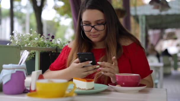 Menina bonito se comunica em um smartphone em uma mesa em um café — Vídeo de Stock