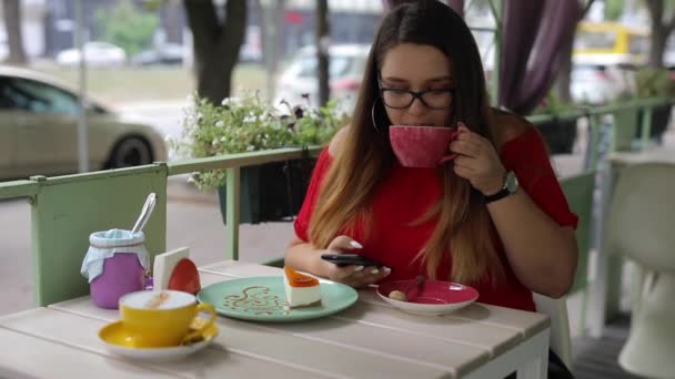 Linda chica se comunica en un teléfono inteligente en una mesa en un café — Vídeo de stock