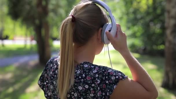 Mujer se pone auriculares en el parque, vista trasera — Vídeos de Stock