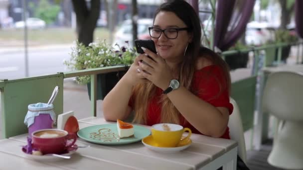 Ragazza carina comunica in uno smartphone a un tavolo in un caffè — Video Stock