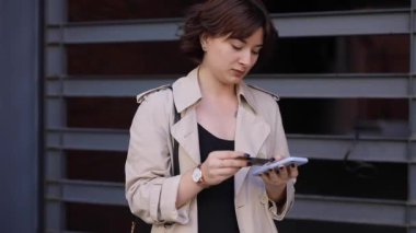 Trençkotla akıllı telefonda sohbet eden hoş bir kadın.