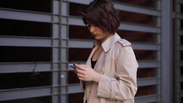 Leuke vrouw chatten in smartphone in trench jas — Stockvideo