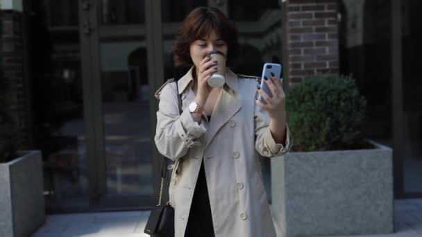 Жінка з коричневим волоссям в тренч пальто балачки по відео чату — стокове відео