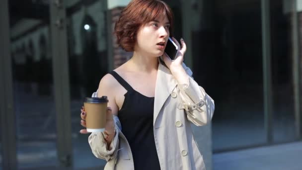 Смішна жінка клянеться своїм хлопцем по телефону в траншеї пальто — стокове відео