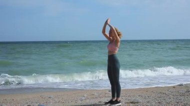 Genç bir kadın okyanus kıyısında meditasyon yapıyor.