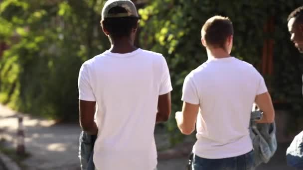 Três amigos multirraciais caminham pela cidade com camisetas brancas — Vídeo de Stock