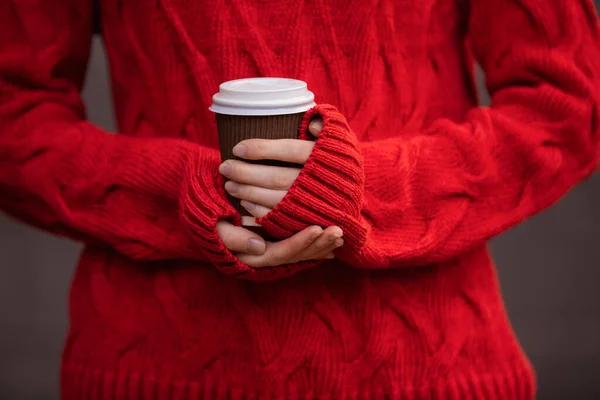 Unrecognizable person in a red pullover holds a cup of hot drink