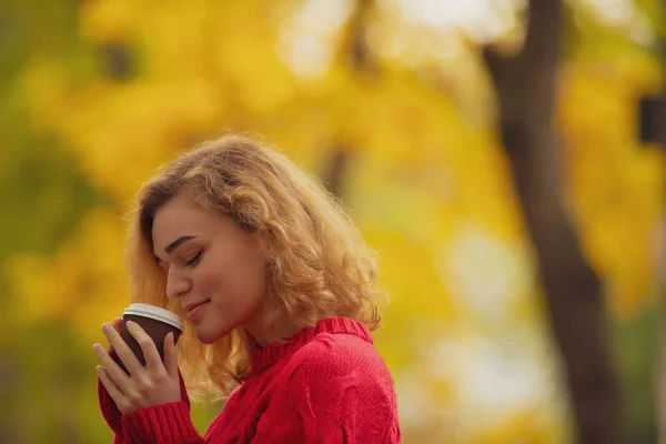 Nette Frau auf gelbem Herbstlaub mit einer Tasse Kaffee — Stockfoto