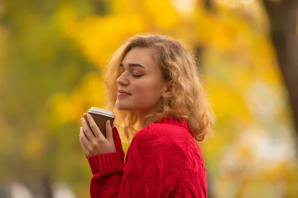 Wanita lucu di latar belakang daun kuning musim gugur dengan secangkir kopi — Stok Foto