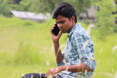 Doğada otururken cep telefonuyla konuşan düşünceli Asyalı genç adam.