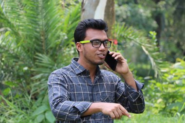 Kot pantolon, tişört ve slayt terlik giyen şık genç Asyalı bir adam bir caddenin ortasında oturup poz veriyor.