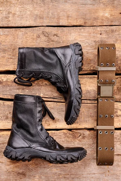 Black army boots and strap on wood.