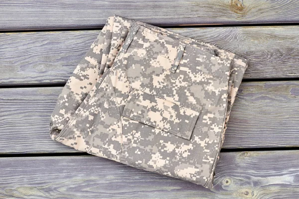 Folded camouflage pants on wood.