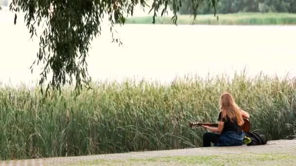 Vrouw spelen een gitaar van de oevers van de rivier. — Stockvideo