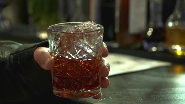 Cerca de mano masculina sosteniendo vaso de brandy con hielo . — Vídeos de Stock