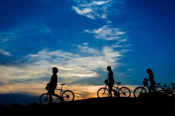 Siluety cyklistů procházky při západu slunce. — Stock fotografie